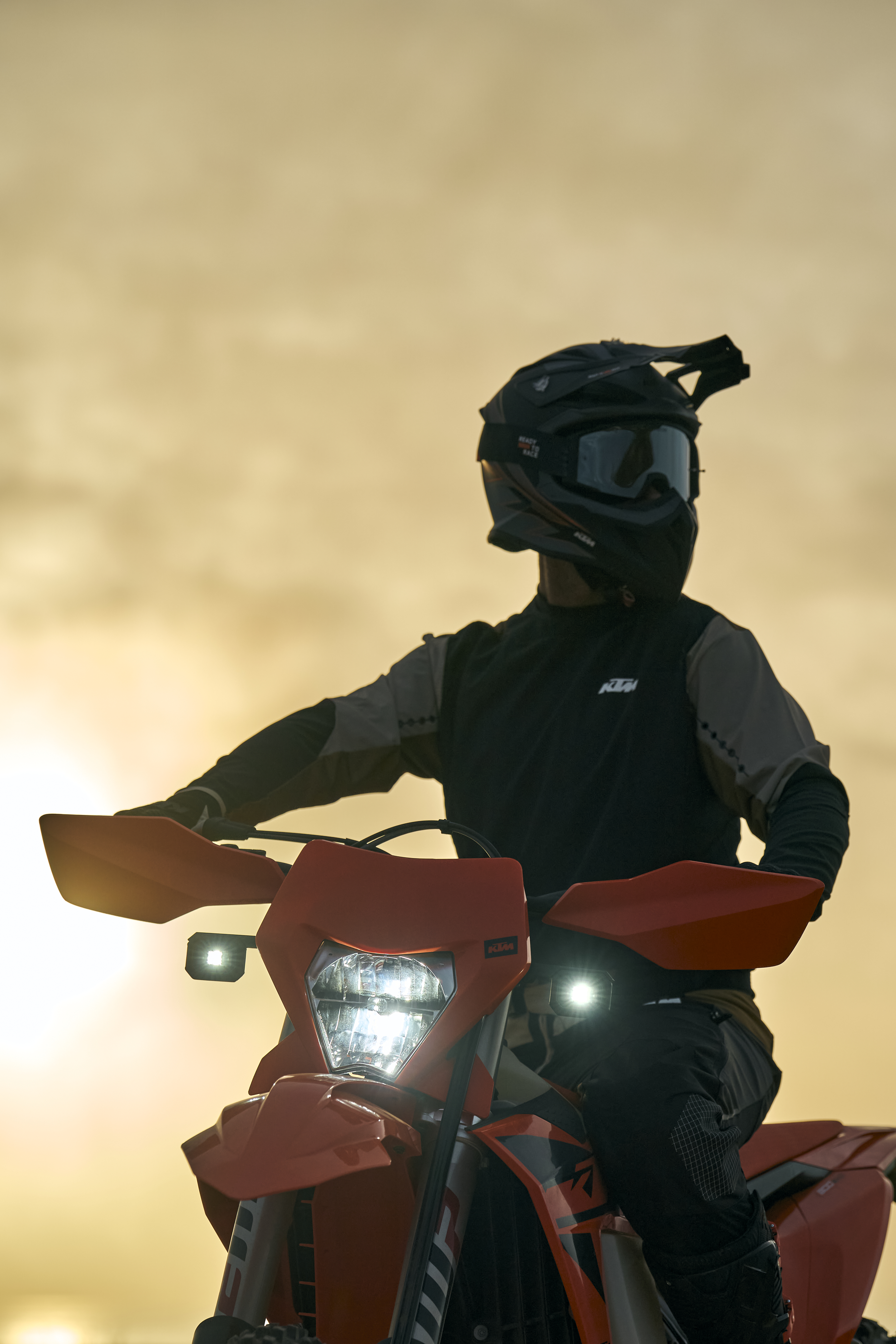 Off-road KTM motorcycle with Baja Designs XL80 LED headlight kit, rider geared up for trail riding at sunrise, high-performance daytime-to-night lighting